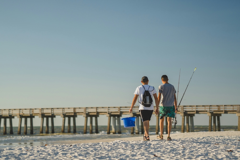 Men with fishing poles in front of a pier.